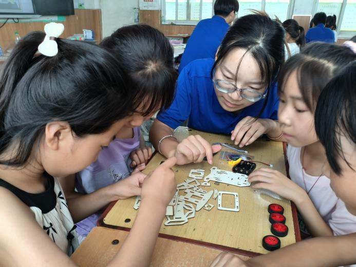 “红”马甲公益科普服务团志愿者在指导小学生组装汽车模型